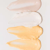 Four samples of skincare creams smeared onto a white background.
