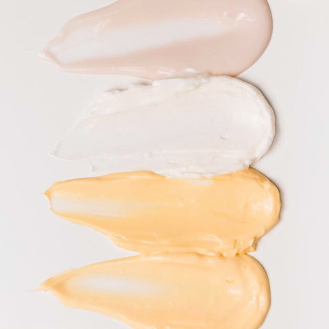 Four samples of skincare creams smeared onto a white background.