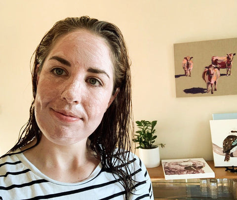 Ladies face painted with pink clay mask at home with paintings in the background.