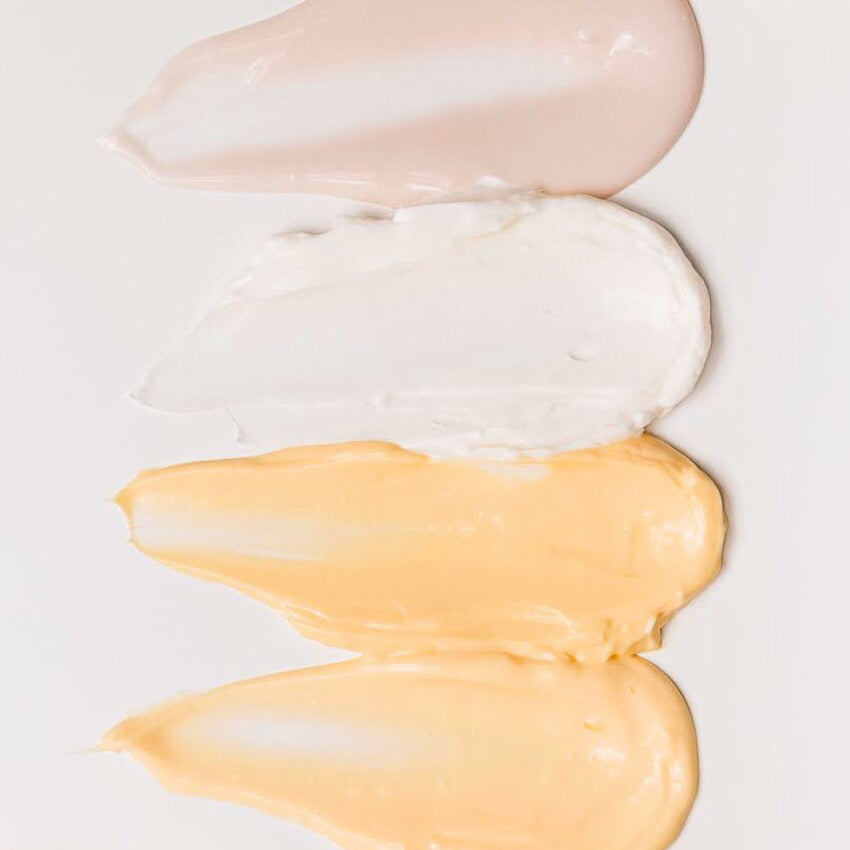 Four samples of skincare creams smeared onto a white background.