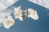 A jar of Essential Eye Cream on a mirrored surface with white flowers.